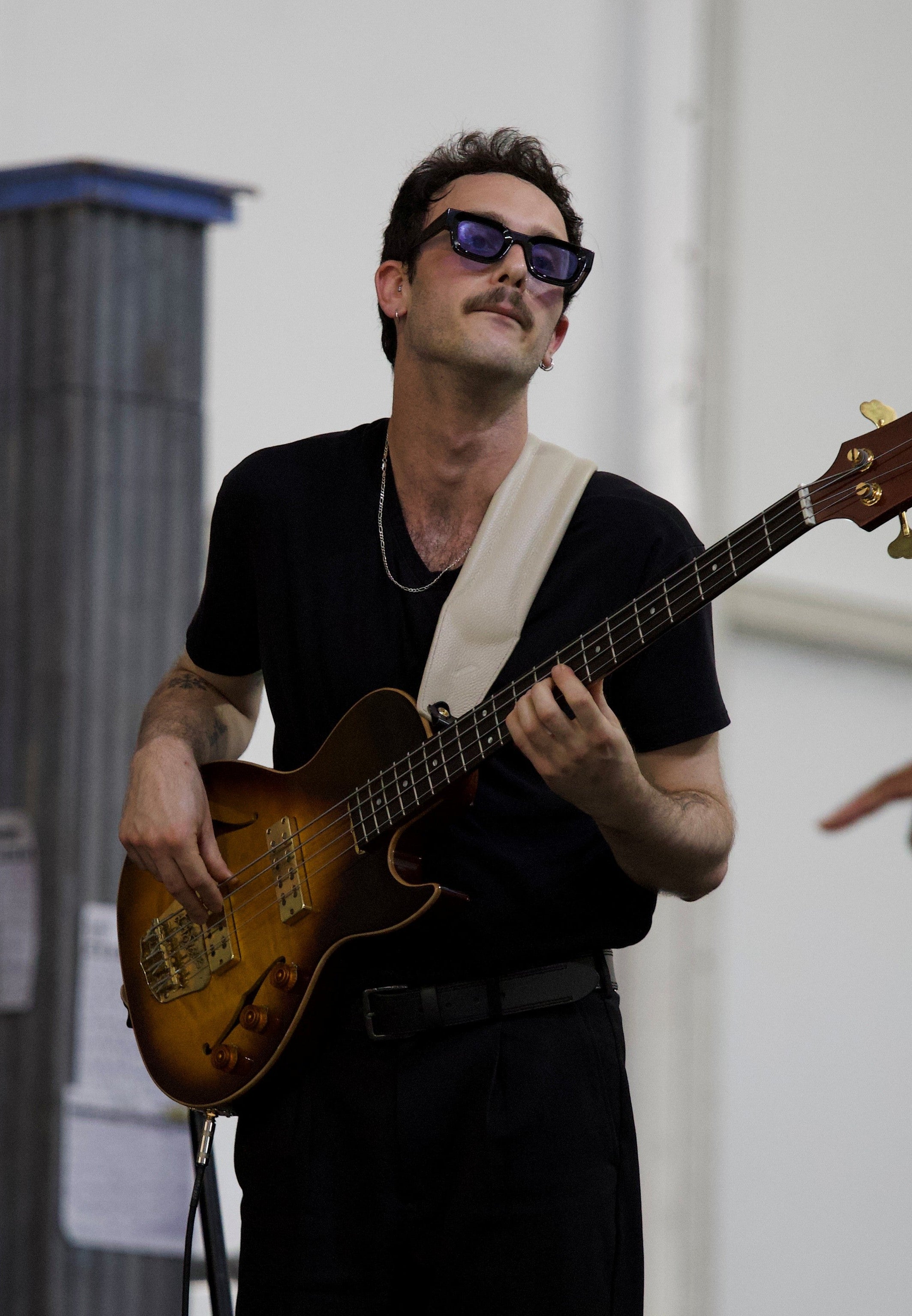 Man playing bass guitar with sunglasses on, wearing a black outfit.